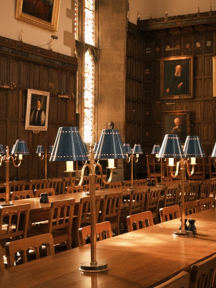 Warm and vintage interior of Oxford's historic dining hall featuring classic wood furniture and vintage lamps.